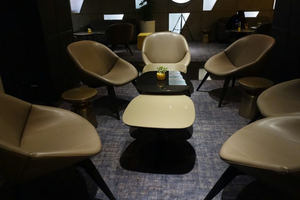 Modern beige armchairs arranged around low tables in a dimly lit lounge